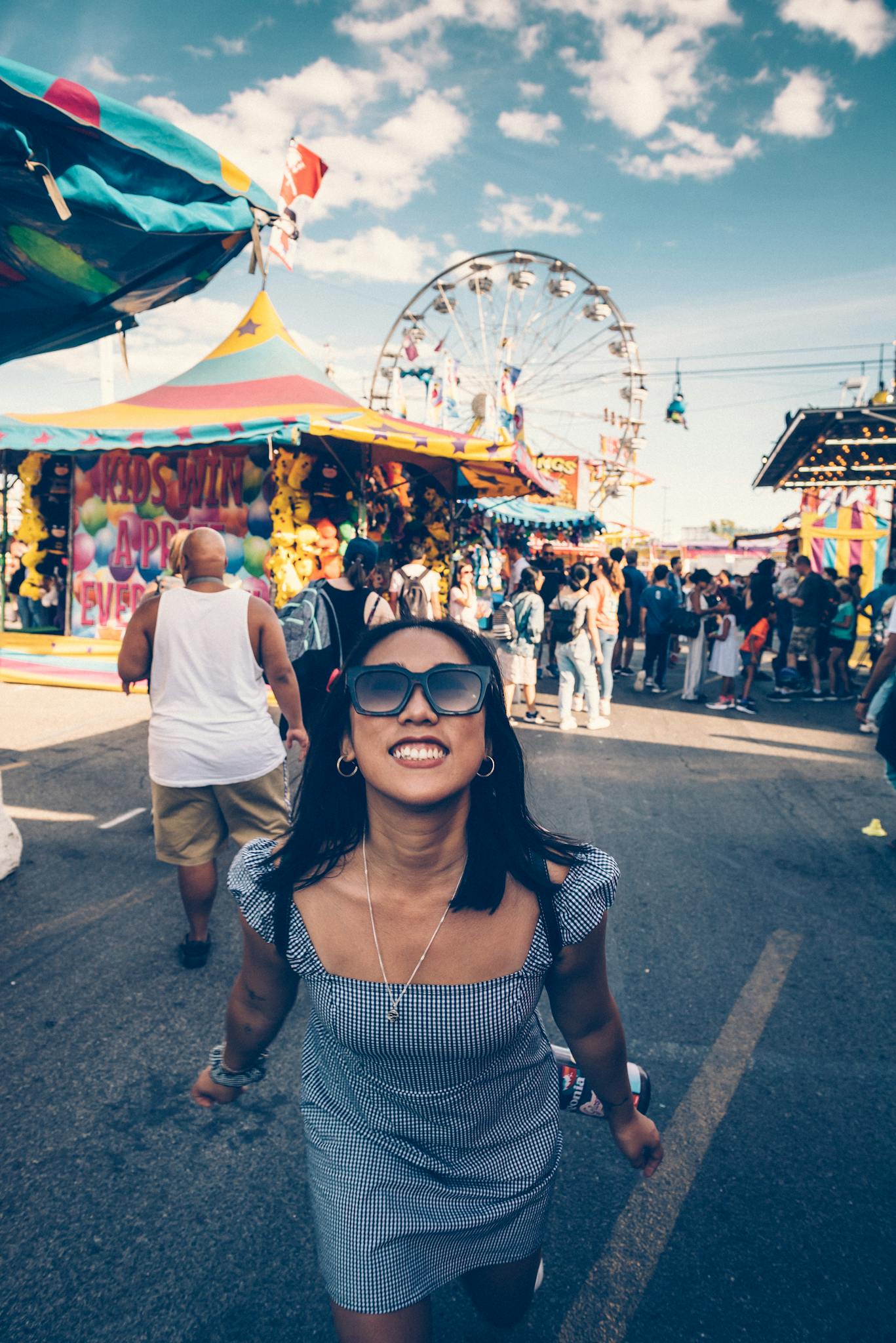 A smiling woman enjoys a lively festival with a ferris wheel in the background.